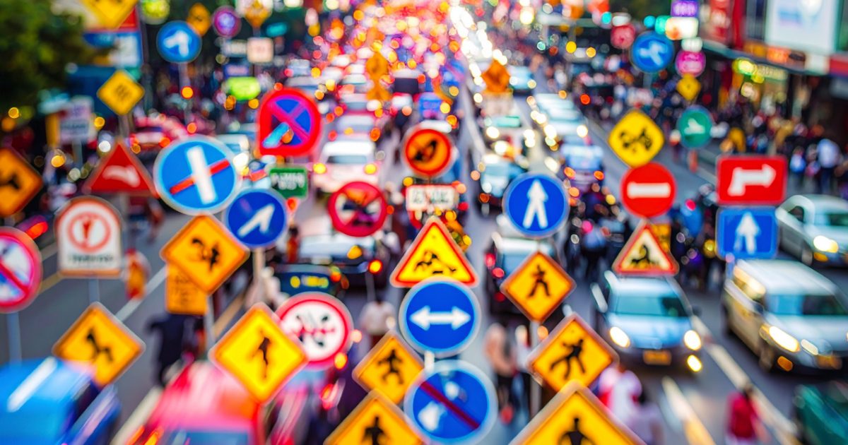 Rue très fréquentée avec une circulation dense avec de nombreux panneaux de signalisation de différentes formes et couleurs. Ils en deviennent illisibles.